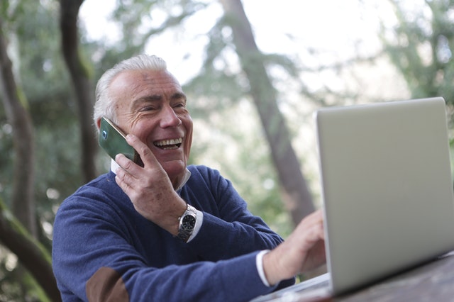 Starší telefonující a smějící se muž sedící před počítačem